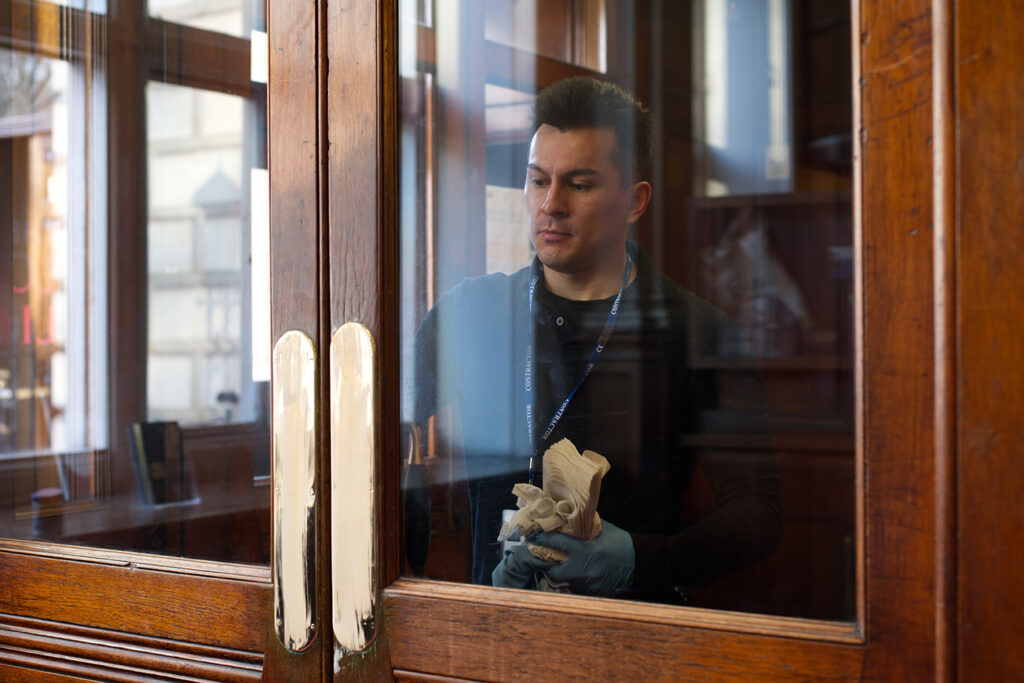 A NuServe operative wiping down a door window.