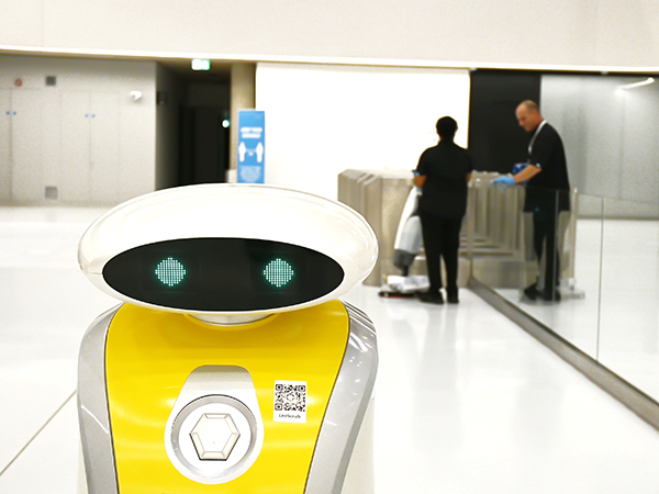 A robotic cleaning machine with cleaners in background.