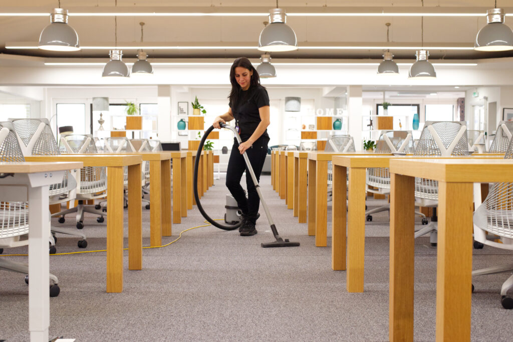 A NuServe operative vacuum cleaning an office carpet.