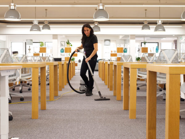 A NuServe operative vacuum cleaning an office carpet.